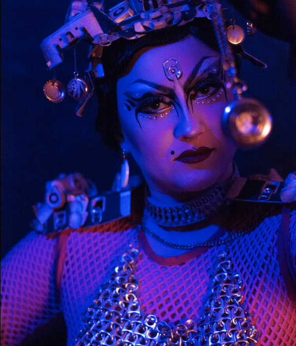 image représentant une drag Queen dans une lumière chaude/rose avec une montre à gousset devant le visage